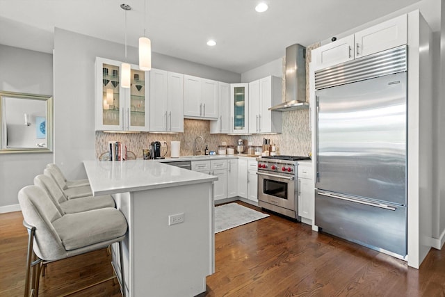 2140 W Armitage Ave Unit 3W, Chicago, IL 60647 - kitchen featuring premium appliances, wall chimney exhaust hood, a peninsula, white cabinets, and backsplash