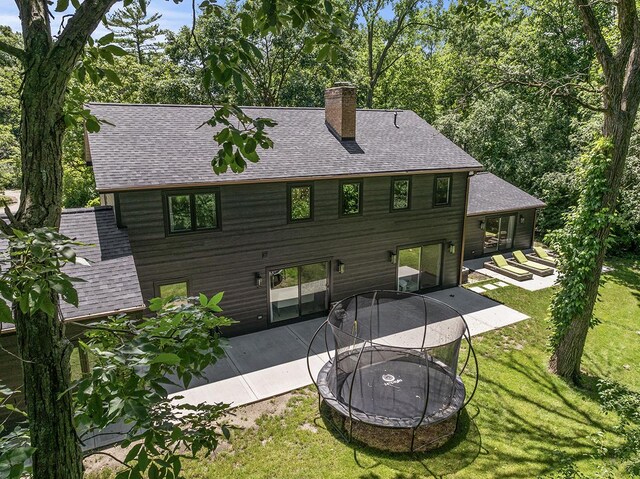 692 S Waukegan Rd, Lake Forest, IL 60045 - back of property with a patio area, roof with shingles, a yard, a chimney, and a trampoline
