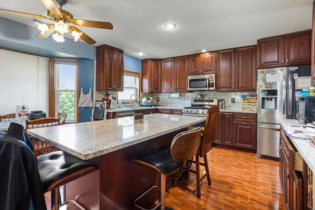 2612 Valkar Ln, Champaign, IL 61822 - kitchen with appliances with stainless steel finishes, a breakfast bar, ceiling fan, a textured ceiling, and decorative backsplash