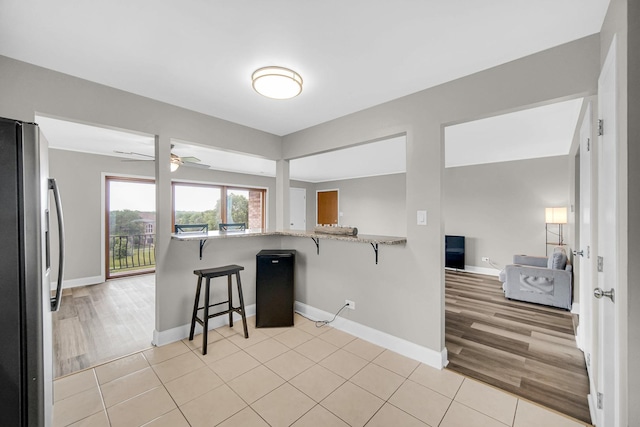 17824 Bernard Dr Unit 3D, Orland Park, IL 60467 - kitchen featuring freestanding refrigerator, a breakfast bar area, ceiling fan, light stone countertops, and light tile patterned floors
