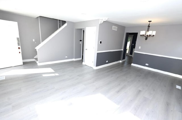 unfurnished living room featuring a chandelier, wood finished floors, and stairs