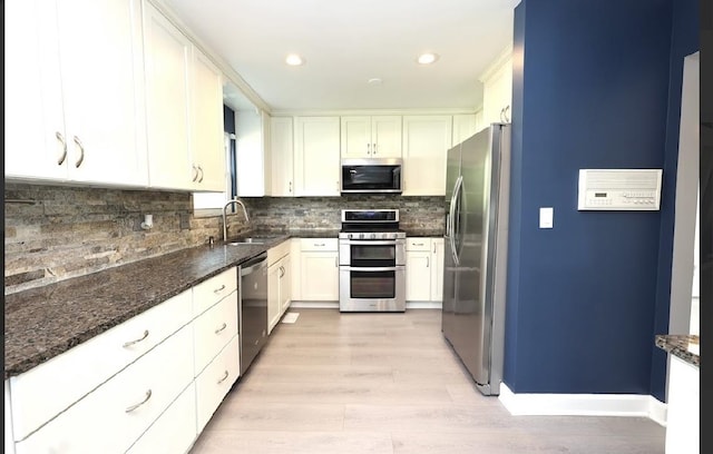 kitchen featuring stainless steel appliances, light wood finished floors, dark stone counters, decorative backsplash, and white cabinets