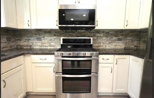 kitchen featuring stainless steel appliances, white cabinets, decorative backsplash, and dark stone countertops