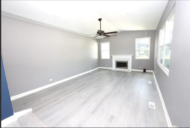 unfurnished living room featuring ceiling fan, light wood-style flooring, a fireplace with flush hearth, and vaulted ceiling
