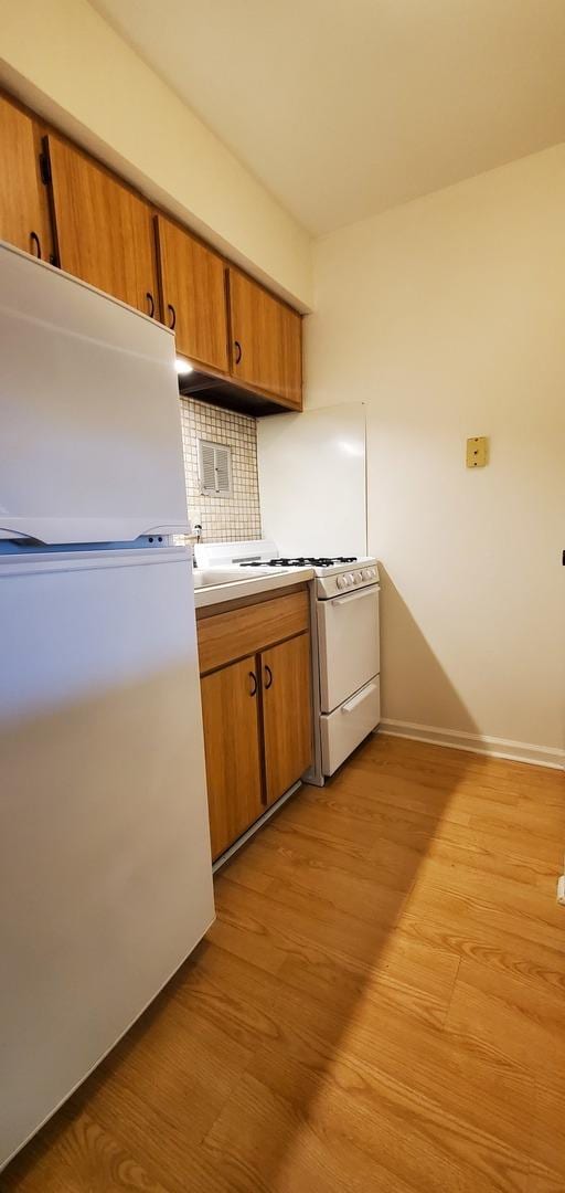 5100 Carriageway Dr Unit 305-2, Rolling Meadows, IL 60008 - kitchen featuring white appliances, light wood finished floors, brown cabinets, tasteful backsplash, and light countertops