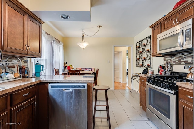 8724 S Jeffery Blvd, Chicago, IL 60617 - kitchen with appliances with stainless steel finishes, decorative backsplash, light tile patterned floors, a peninsula, and hanging light fixtures