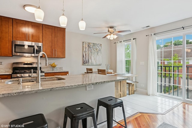 926 Bromley Pl, Northbrook, IL 60062 - kitchen with appliances with stainless steel finishes, brown cabinetry, pendant lighting, light wood-style floors, and a breakfast bar area