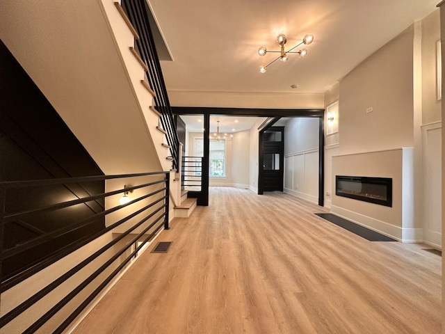 4409 S Prairie Ave, Chicago, IL 60653 - unfurnished living room featuring a chandelier, light wood finished floors, stairs, a decorative wall, and a glass covered fireplace
