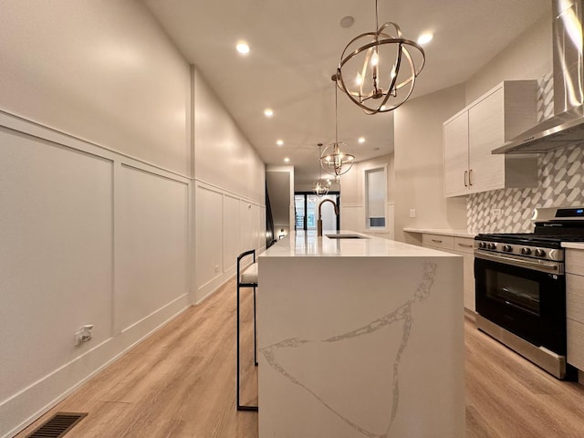 4409 S Prairie Ave, Chicago, IL 60653 - kitchen featuring stainless steel gas range, wall chimney exhaust hood, a chandelier, light wood-style floors, and decorative backsplash