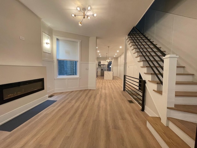 4409 S Prairie Ave, Chicago, IL 60653 - unfurnished living room with a glass covered fireplace, a chandelier, light wood-type flooring, stairs, and a decorative wall