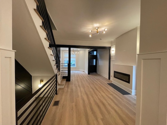 4409 S Prairie Ave, Chicago, IL 60653 - unfurnished living room with a chandelier, stairway, a decorative wall, light wood-style floors, and a glass covered fireplace