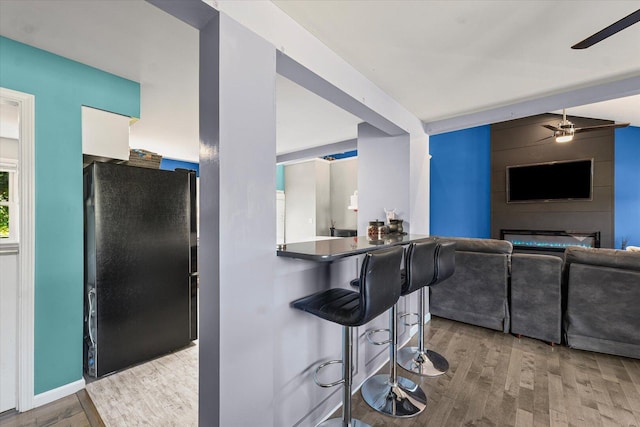 501 N Center St, Colfax, IL 61728 - kitchen featuring freestanding refrigerator, wood finished floors, a kitchen bar, ceiling fan, and a fireplace