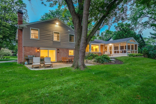 560 Golf Ln, Lake Forest, IL 60045 - back of property at dusk with a chimney, a patio, a sunroom, brick siding, and a yard