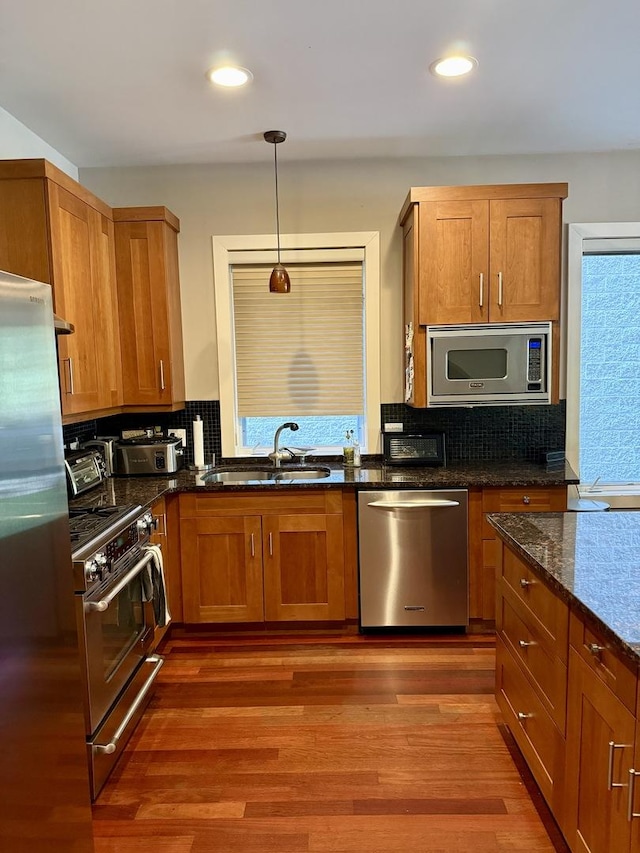 1621 W Le Moyne St Unit 1W, Chicago, IL 60622 - kitchen with stainless steel appliances, brown cabinetry, dark stone counters, backsplash, and wood finished floors