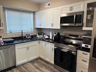9388 Bay Colony Dr Unit 1S, Des Plaines, IL 60016 - kitchen featuring stainless steel appliances, dark countertops, white cabinetry, wood finished floors, and glass insert cabinets