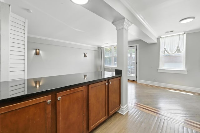 2501 W Touhy Ave Unit 105, Chicago, IL 60645 - kitchen with light wood-style floors, crown molding, brown cabinetry, dark countertops, and ornate columns