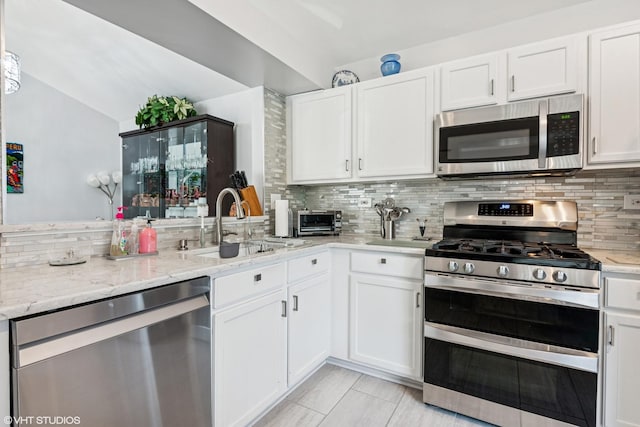 201 Hidden Creek Ln Unit 201, North Aurora, IL 60542 - kitchen featuring appliances with stainless steel finishes, tasteful backsplash, white cabinetry, light stone countertops, and vaulted ceiling