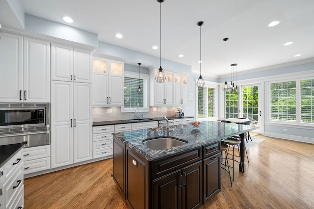 2115 Washington Ave, Wilmette, IL 60091 - kitchen featuring stainless steel microwave, a warming drawer, light wood-style floors, a kitchen bar, and glass insert cabinets
