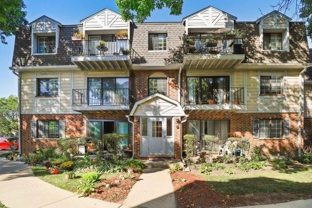 3256 Sanders Rd Unit 4E, Northbrook, IL 60062 - view of property with a balcony, brick siding, a shingled roof, and mansard roof