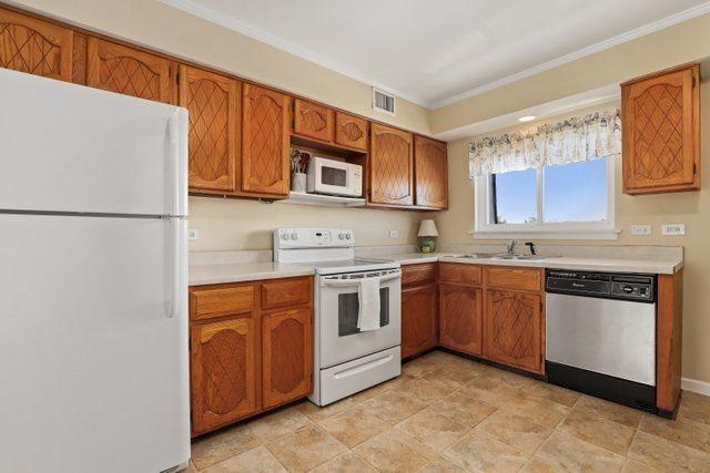 3256 Sanders Rd Unit 4E, Northbrook, IL 60062 - kitchen featuring white appliances, crown molding, brown cabinetry, light countertops, and stone finish floors