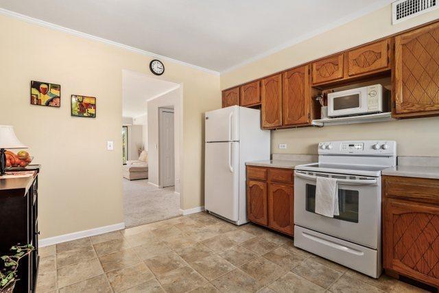 3256 Sanders Rd Unit 4E, Northbrook, IL 60062 - kitchen with white appliances, brown cabinetry, light countertops, stone finish floors, and ornamental molding