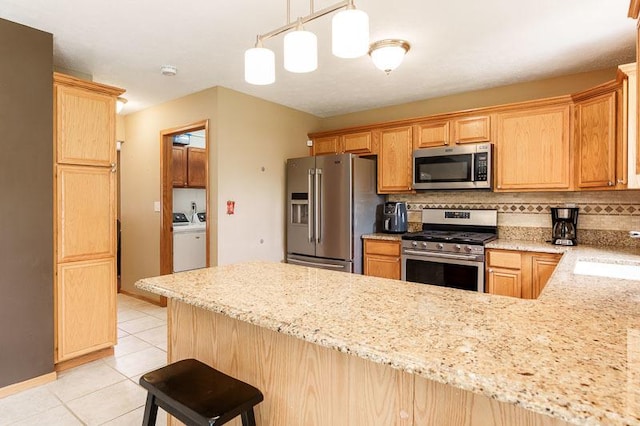 10873 Meadowsweet Ln, Roscoe, IL 61073 - kitchen with appliances with stainless steel finishes, washing machine and clothes dryer, light tile patterned floors, decorative backsplash, and a peninsula