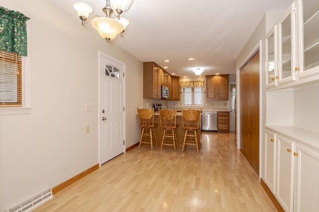1316 Kirkwood Dr, Pontiac, IL 61764 - kitchen with stainless steel appliances, brown cabinets, light wood-style flooring, glass insert cabinets, and a chandelier