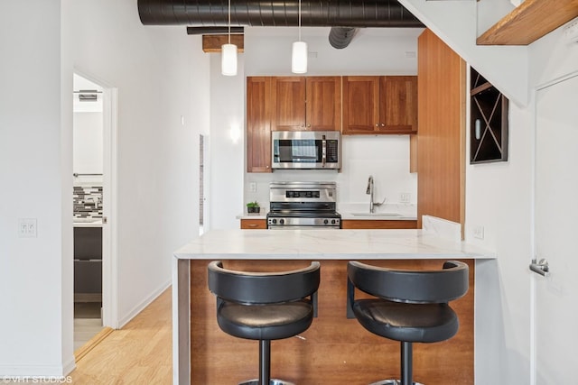 331 S Peoria St Unit Ph6, Chicago, IL 60607 - kitchen with stainless steel appliances, brown cabinetry, a breakfast bar area, a peninsula, and decorative light fixtures