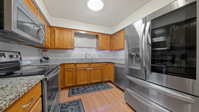 5715 Elaine Dr, Rockford, IL 61108 - kitchen with appliances with stainless steel finishes, brown cabinets, light wood finished floors, a textured ceiling, and light stone countertops