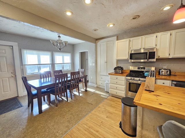 320 Congress St, Ottawa, IL 61350 - kitchen with butcher block countertops, stainless steel appliances, a chandelier, white cabinets, and pendant lighting
