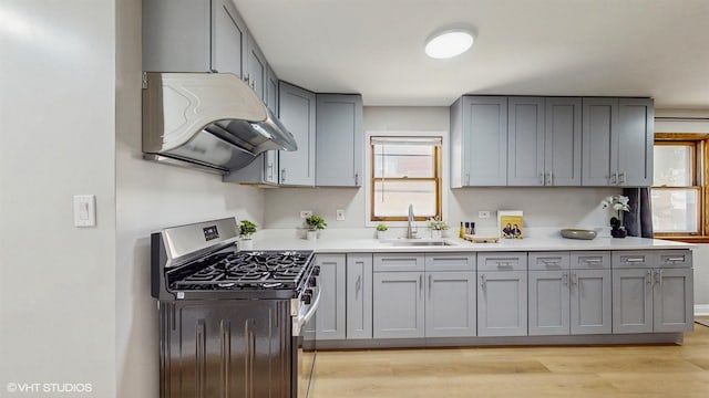 2701 S Hillock Ave, Chicago, IL 60608 - kitchen featuring stainless steel gas range oven, range hood, gray cabinetry, light wood-style flooring, and plenty of natural light