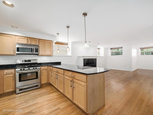 4411 N Beacon St Unit G, Chicago, IL 60640 - kitchen featuring appliances with stainless steel finishes, dark countertops, a peninsula, light wood-type flooring, and open floor plan