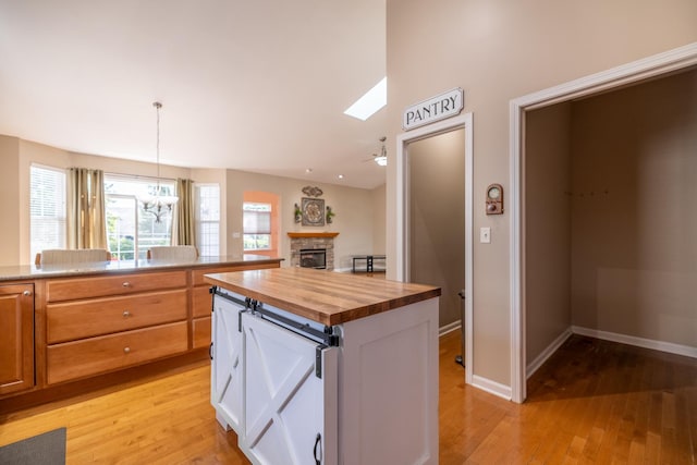 424 Riverbend Dr, Genoa, IL 60135 - kitchen with butcher block counters, light wood-style flooring, a fireplace, white cabinets, and hanging light fixtures