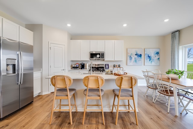 1039 Greenleaf St, Sycamore, IL 60178 - kitchen with appliances with stainless steel finishes, light wood finished floors, light countertops, a kitchen breakfast bar, and white cabinetry