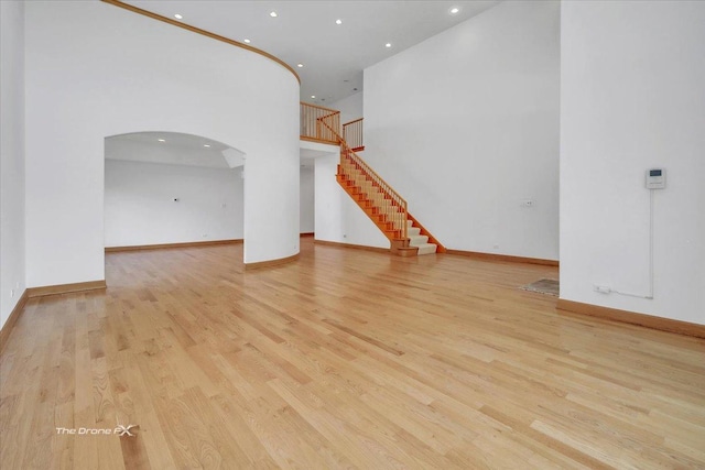 3550 E Ari Dr, Glenview, IL 60025 - unfurnished living room with recessed lighting, arched walkways, light wood-type flooring, stairway, and a towering ceiling