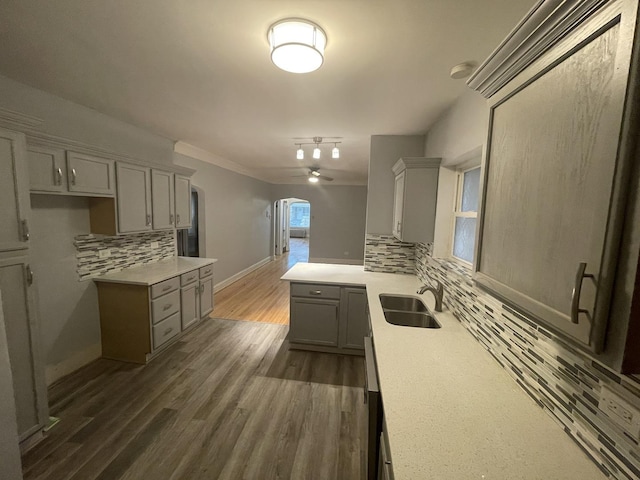 kitchen featuring arched walkways, gray cabinetry, decorative backsplash, light countertops, and ornamental molding
