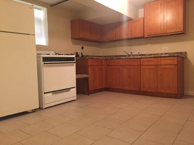 kitchen featuring stove, freestanding refrigerator, brown cabinets, and dark countertops