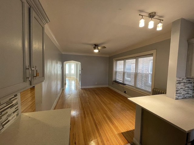 unfurnished living room with arched walkways, ornamental molding, ceiling fan, and light wood-style floors