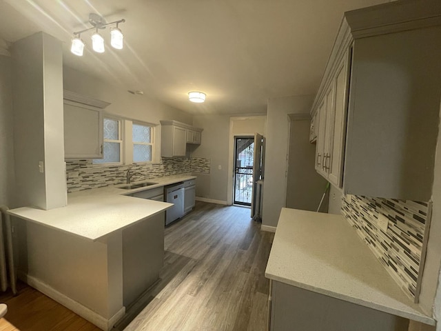 kitchen featuring tasteful backsplash, dishwasher, a peninsula, and wood finished floors