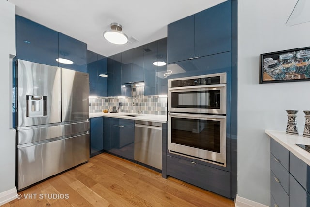 130 N Garland Ct Unit 2612, Chicago, IL 60602 - kitchen featuring appliances with stainless steel finishes, blue cabinetry, light wood-style floors, and decorative backsplash