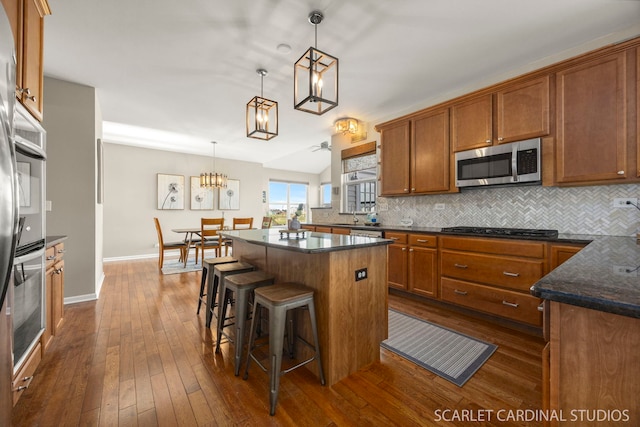 854 Preston Ln, Oswego, IL 60543 - kitchen featuring stainless steel microwave, tasteful backsplash, brown cabinets, a center island, and black cooktop