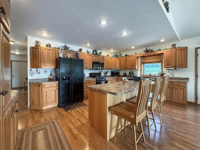 5782 N Brown Rd, Dakota, IL 61018 - kitchen with black appliances, light wood-style flooring, a textured ceiling, a kitchen breakfast bar, and brown cabinetry