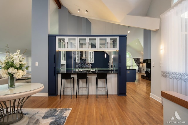 113 Oak Ridge Dr E, Burr Ridge, IL 60527 - kitchen with dark countertops, light wood-type flooring, a kitchen breakfast bar, high vaulted ceiling, and glass insert cabinets