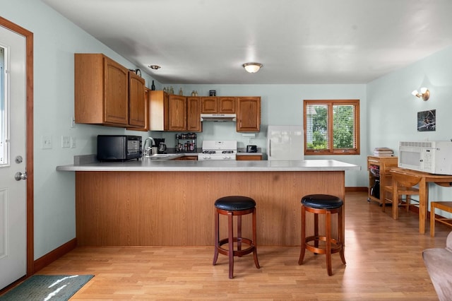 101 W Olive St, Colfax, IL 61728 - kitchen with white gas stove, a peninsula, under cabinet range hood, light wood-type flooring, and light countertops