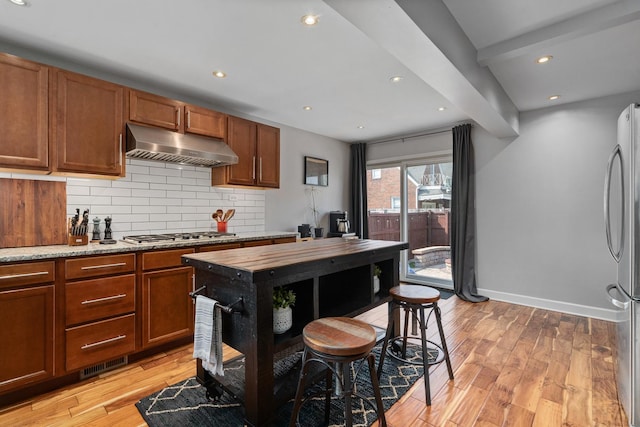 592 E 13th St, Lockport, IL 60441 - kitchen with under cabinet range hood, stainless steel appliances, light wood-style floors, tasteful backsplash, and brown cabinetry