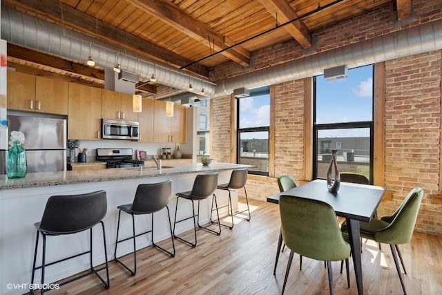 2511 W Moffat St Unit 305-D, Chicago, IL 60647 - kitchen featuring appliances with stainless steel finishes, brick wall, a wood ceiling with exposed beams, light wood-style flooring, and light stone counters