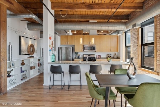 2511 W Moffat St Unit 305-D, Chicago, IL 60647 - kitchen with stainless steel appliances, a wood ceiling with exposed beams, light wood-style flooring, a breakfast bar, and light stone counters