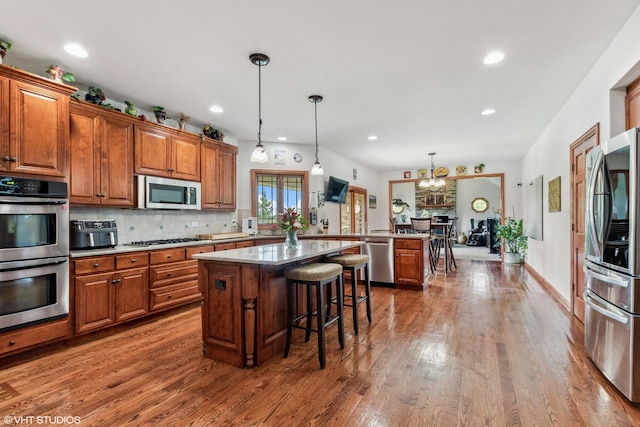 9265 Maura Ct, Frankfort, IL 60423 - kitchen with appliances with stainless steel finishes, brown cabinetry, wood finished floors, a kitchen island, and a kitchen bar