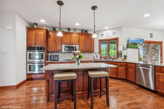 9265 Maura Ct, Frankfort, IL 60423 - kitchen with appliances with stainless steel finishes, wood finished floors, brown cabinetry, a breakfast bar area, and recessed lighting