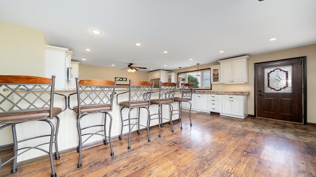 18521 Anderson Rd, Prophetstown, IL 61277 - kitchen featuring a ceiling fan, a breakfast bar area, a peninsula, wood finished floors, and glass insert cabinets